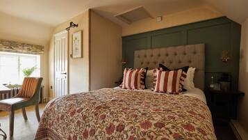 A bedroom with a large bed, a chair, a desk, and a door.