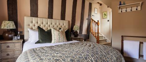 A bedroom with a large bed, a nightstand, a lamp, a dresser, and a staircase.