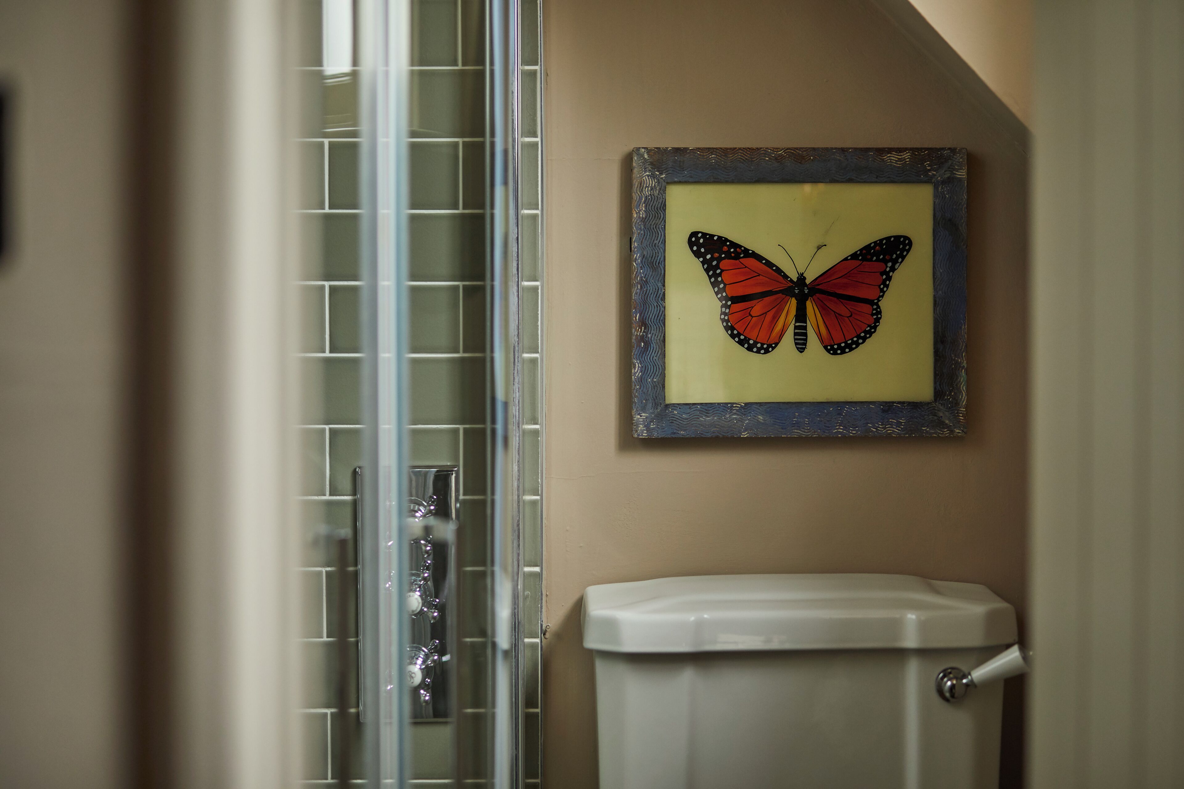 A bathroom with a glass shower enclosure, a toilet, and a framed butterfly artwork on the wall.