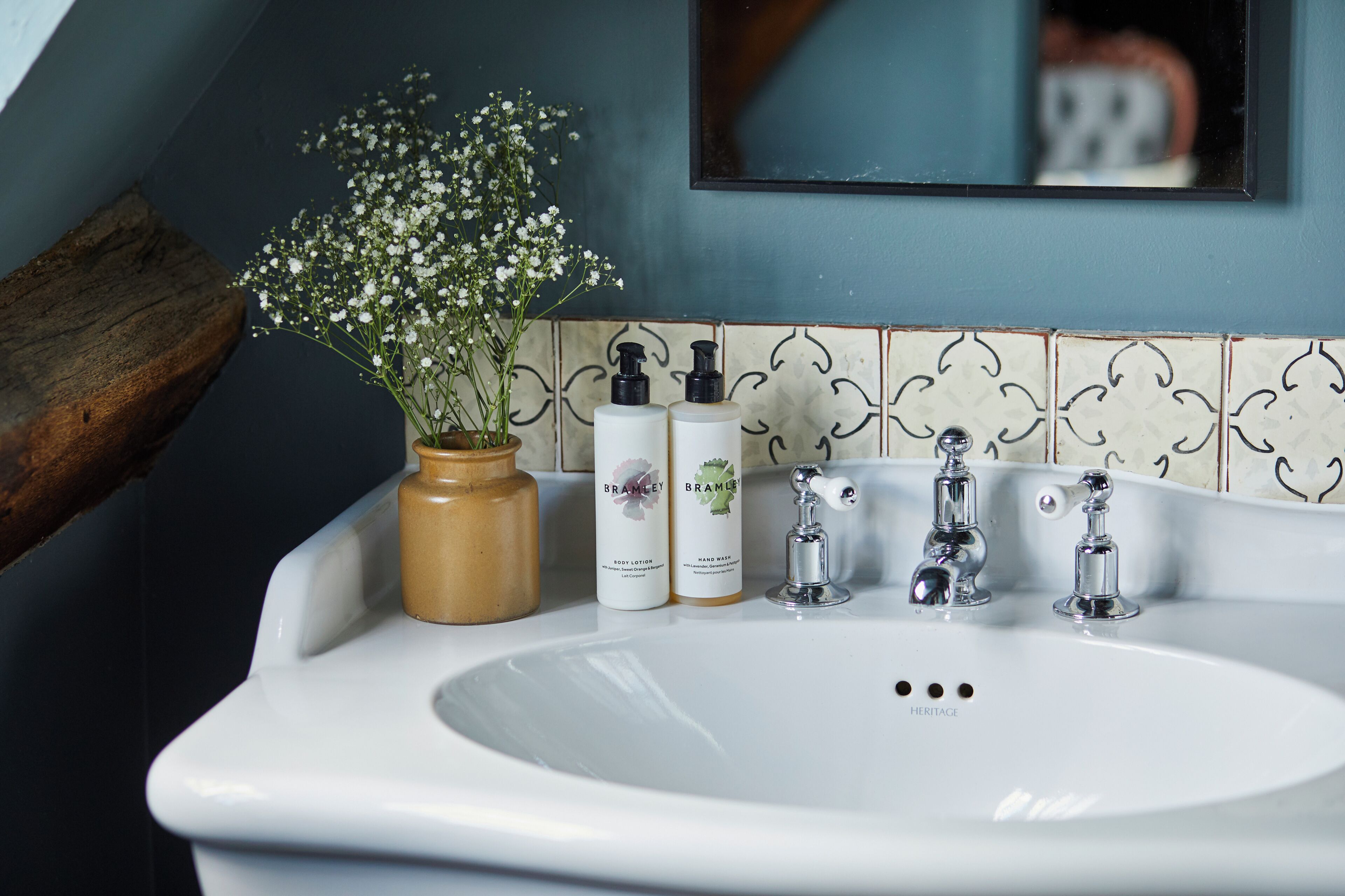 A bathroom sink with a vase of flowers, two bottles of lotion, and a mirror above.