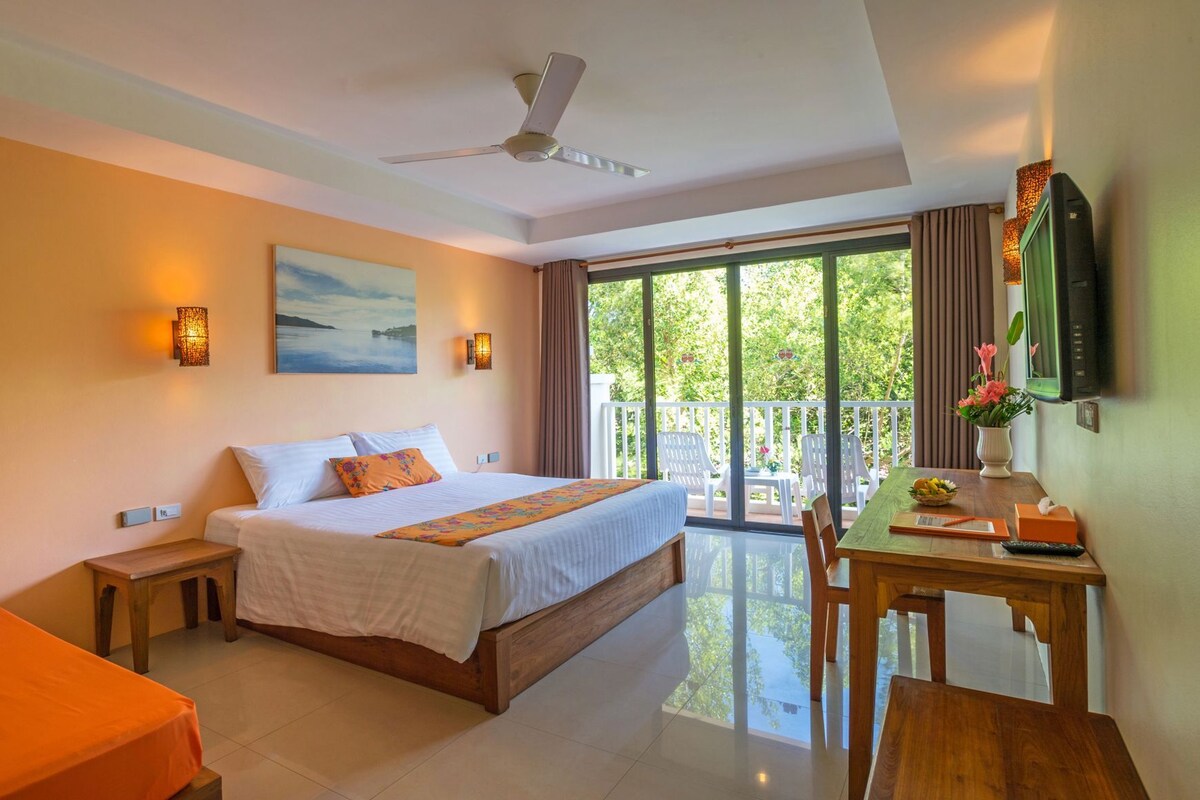 A hotel room with a bed, a desk with a chair, a balcony with a view, and a ceiling fan.