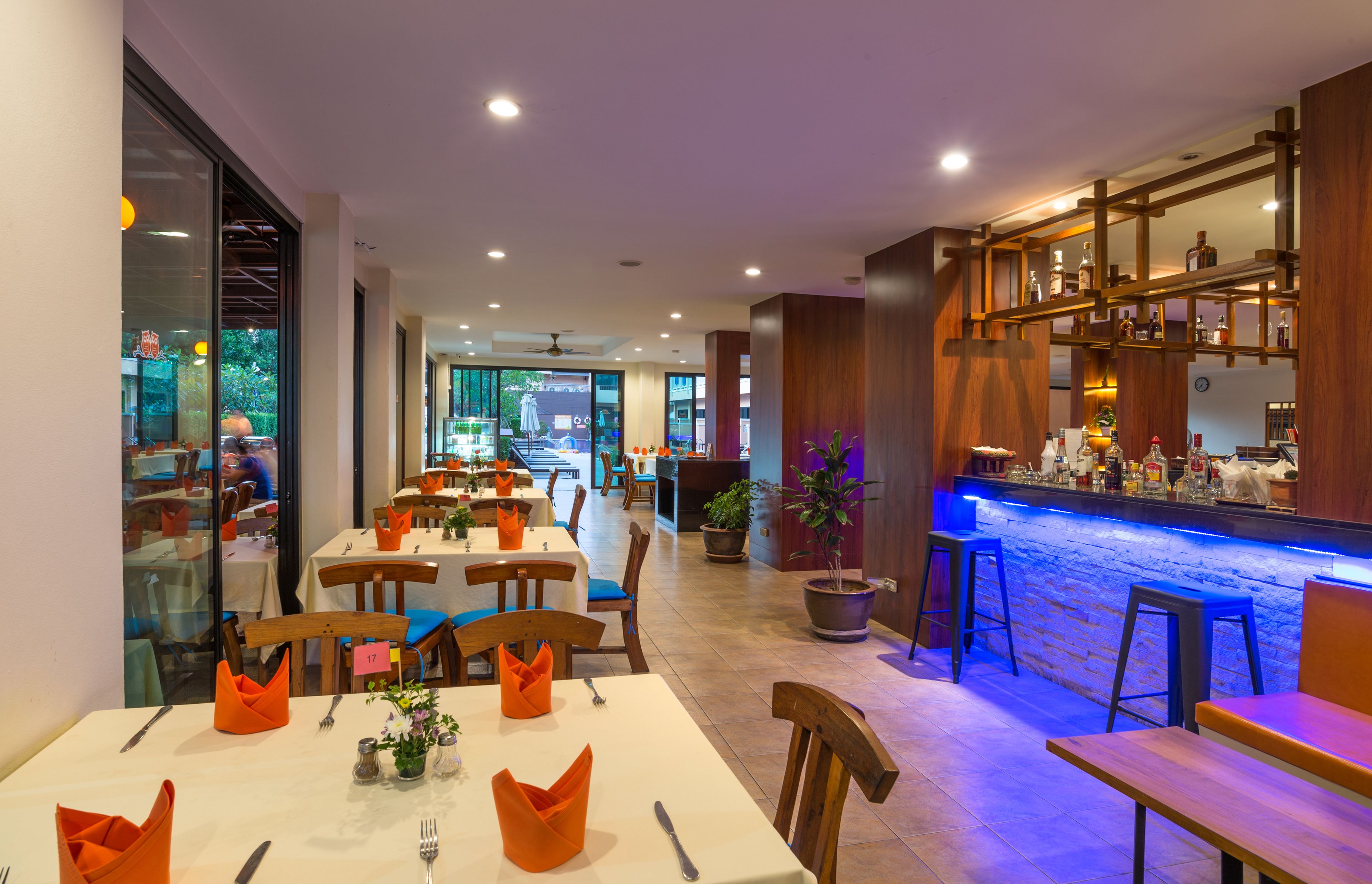 A restaurant with tables set for dining, a bar area with stools, and a view of the street outside.