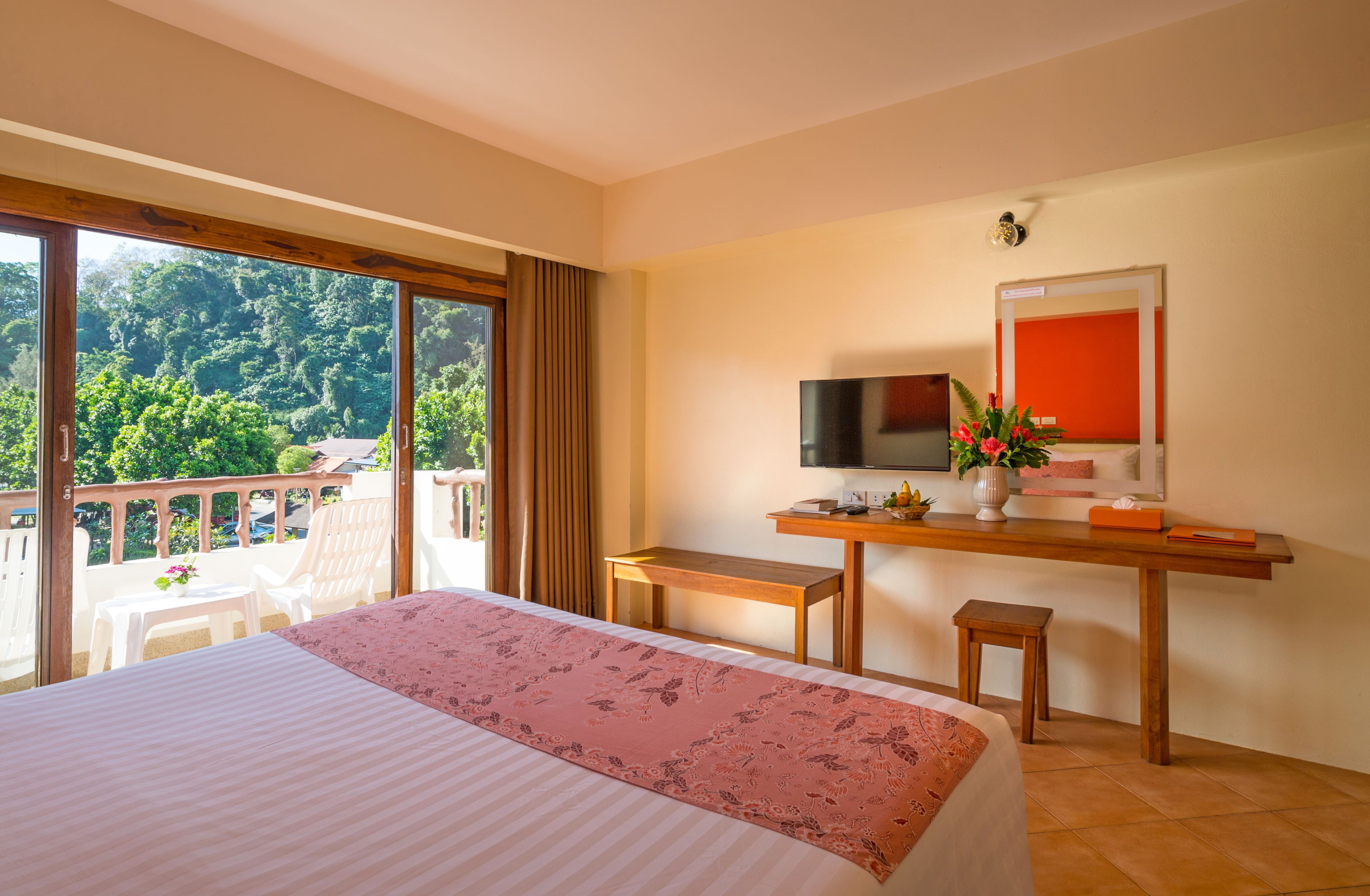Hotelkamer met een groot bed, een bureau met een televisie en een balkon met uitzicht op het bos.