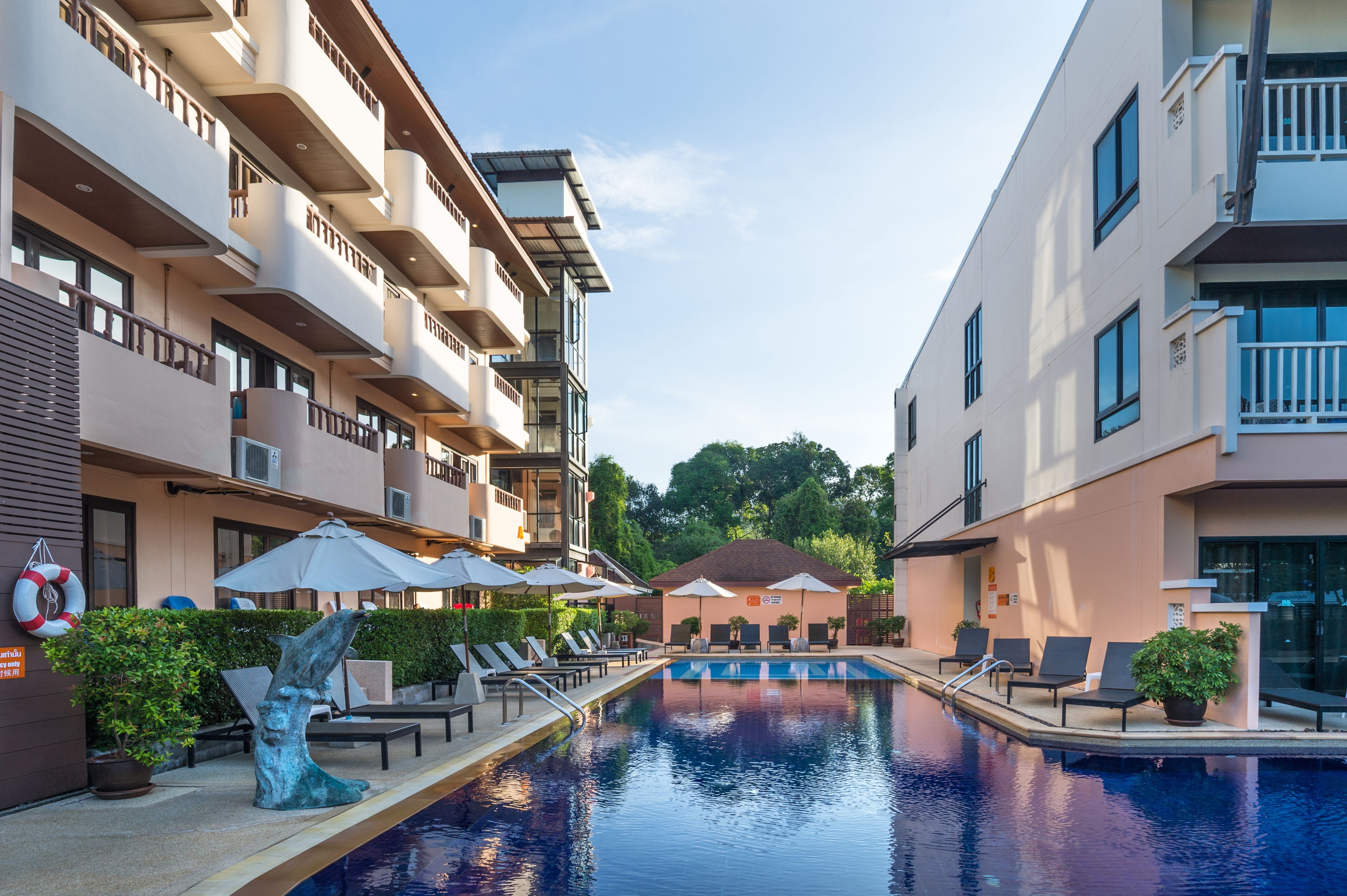 Une piscine entourée de bâtiments à plusieurs étages dotés de balcons, avec des chaises longues et des parasols, et une bouée de sauvetage posée sur le sol.