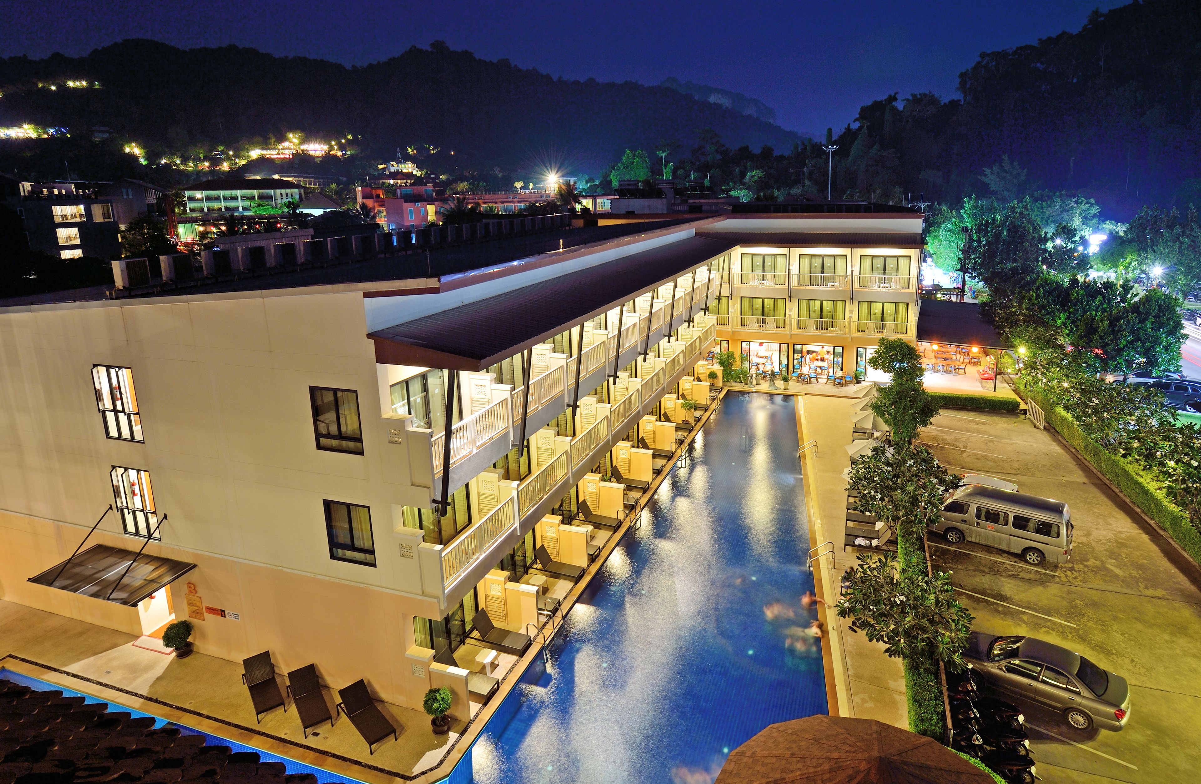 Un hotel con piscina, varios balcones y zona de estacionamiento.