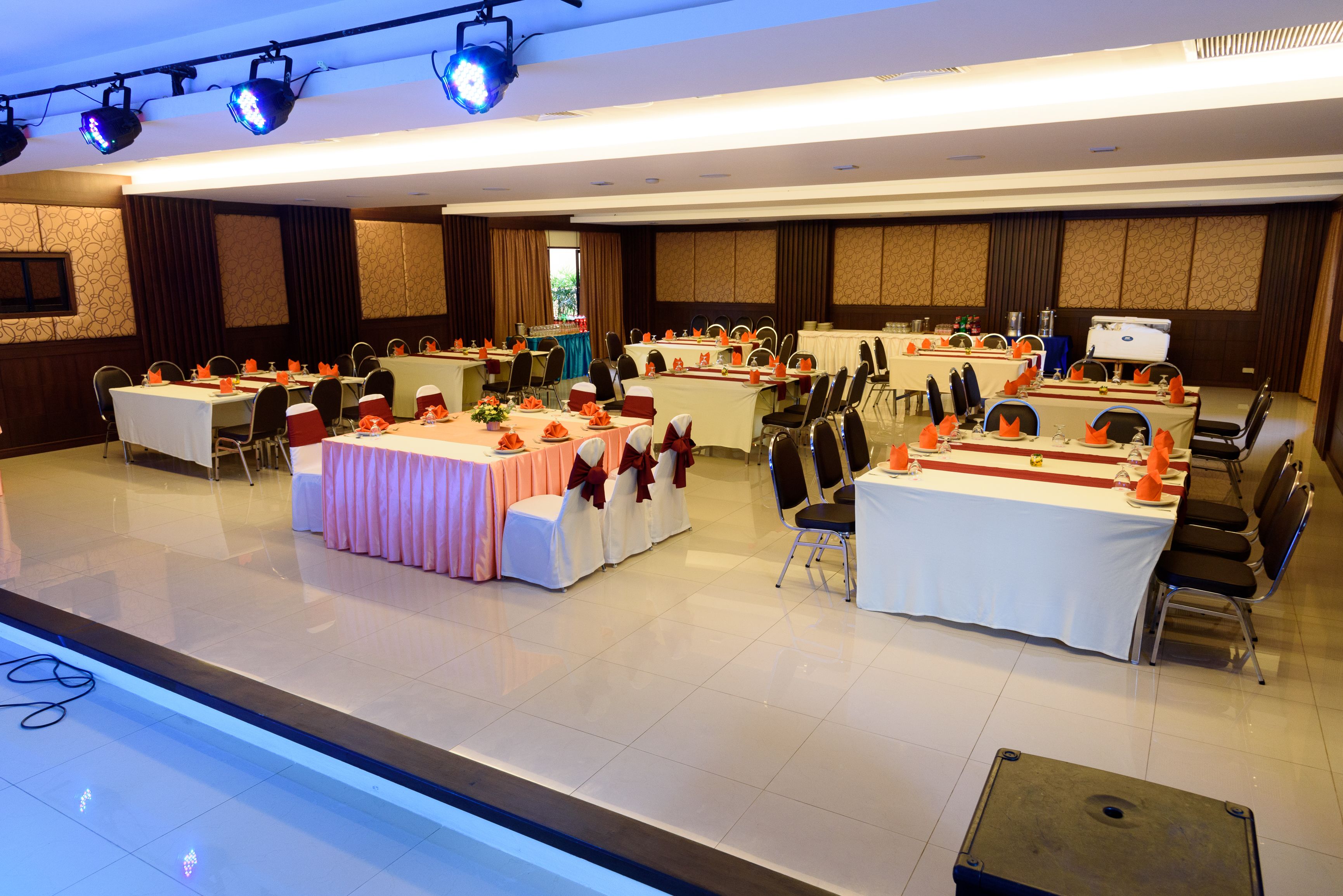 Une salle de conférence équipée de plusieurs tables, de chaises et d’une scène avec un système d’éclairage.