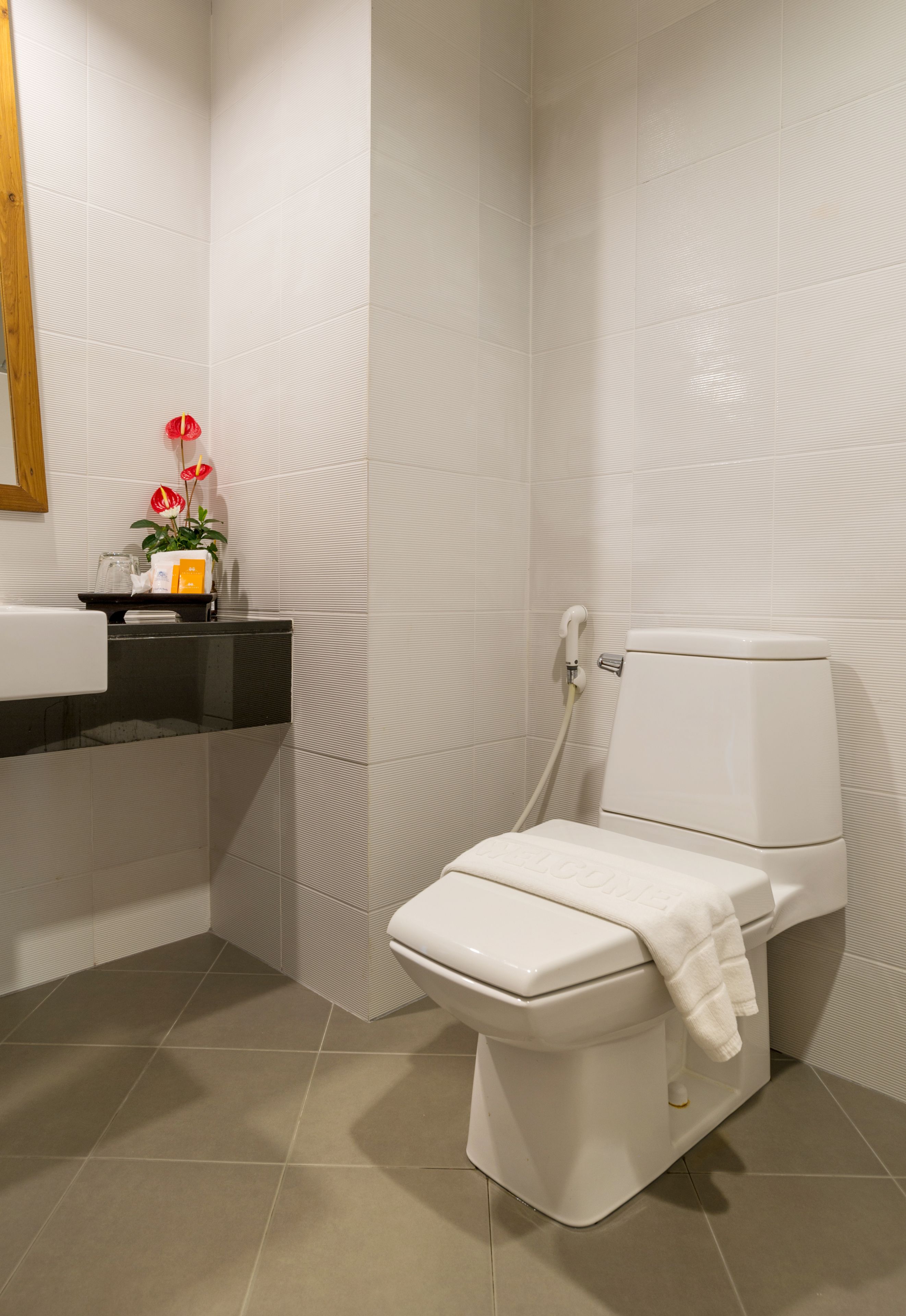 Un baño moderno con inodoro blanco, encimera negra y una planta pequeña con flores rojas.