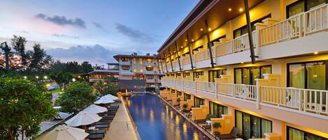 Un hotel con piscina, mobiliario exterior y varios balcones.