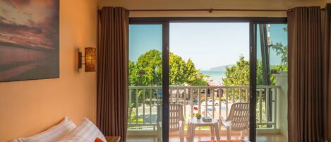 A hotel room with a bed, a painting on the wall, a balcony with a view of the sea, and a table with chairs.