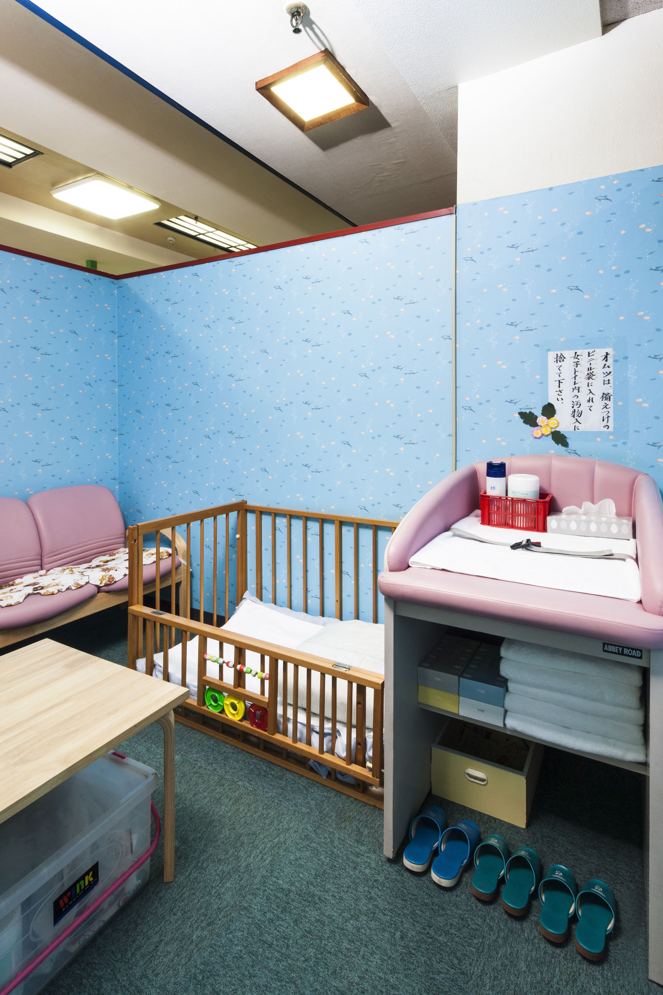 A child's room with a crib, a pink sofa, a wooden table, and a storage unit with shoes.