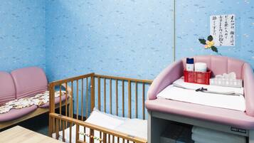 A child's room with a crib, a pink sofa, a wooden table, and a storage unit with shoes.