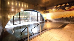 Un espace piscine intérieur moderne, doté d’un mur en verre, de rampes en métal et d’un sol carrelé.