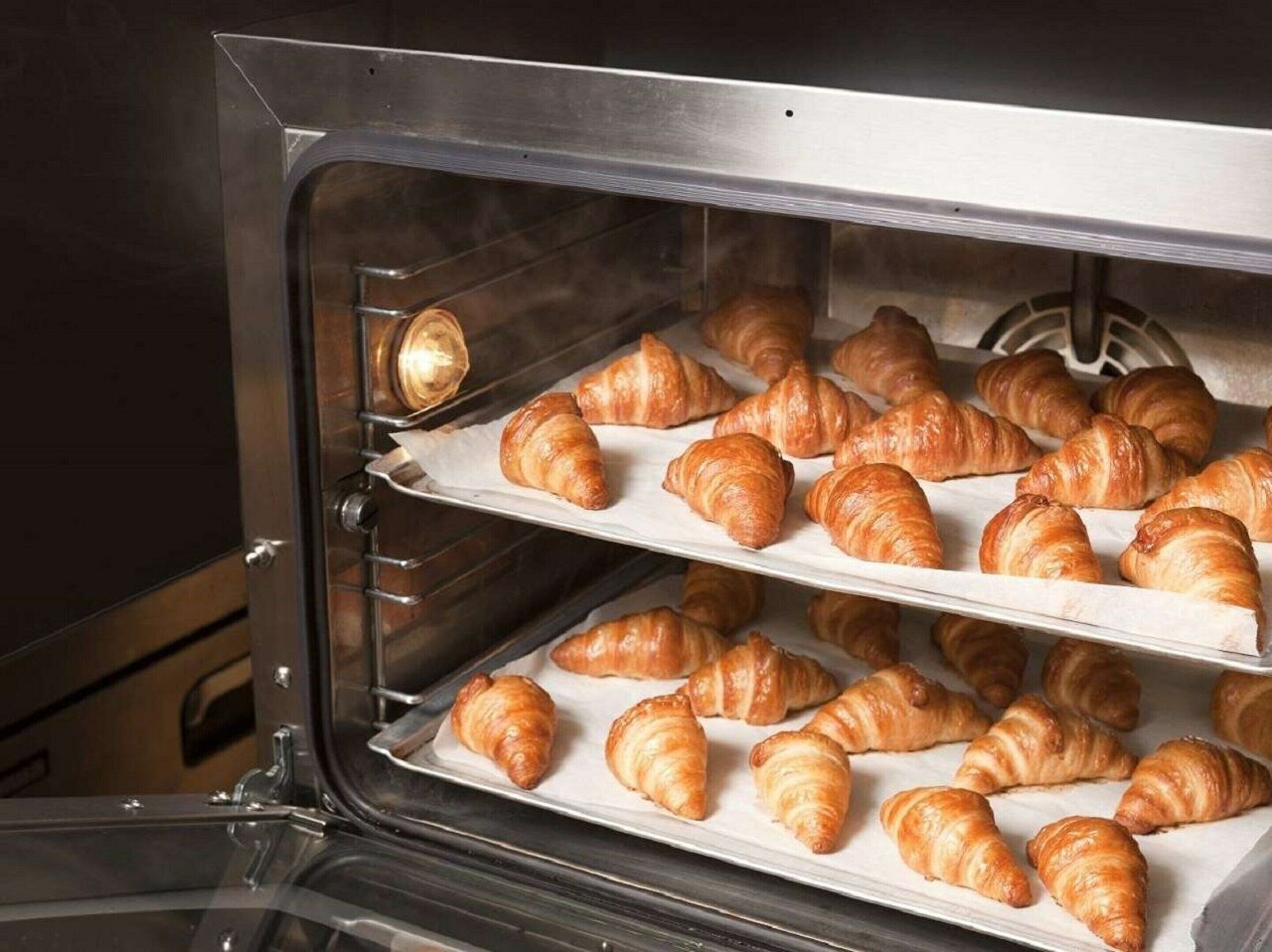 An oven with multiple shelves filled with croissants.
