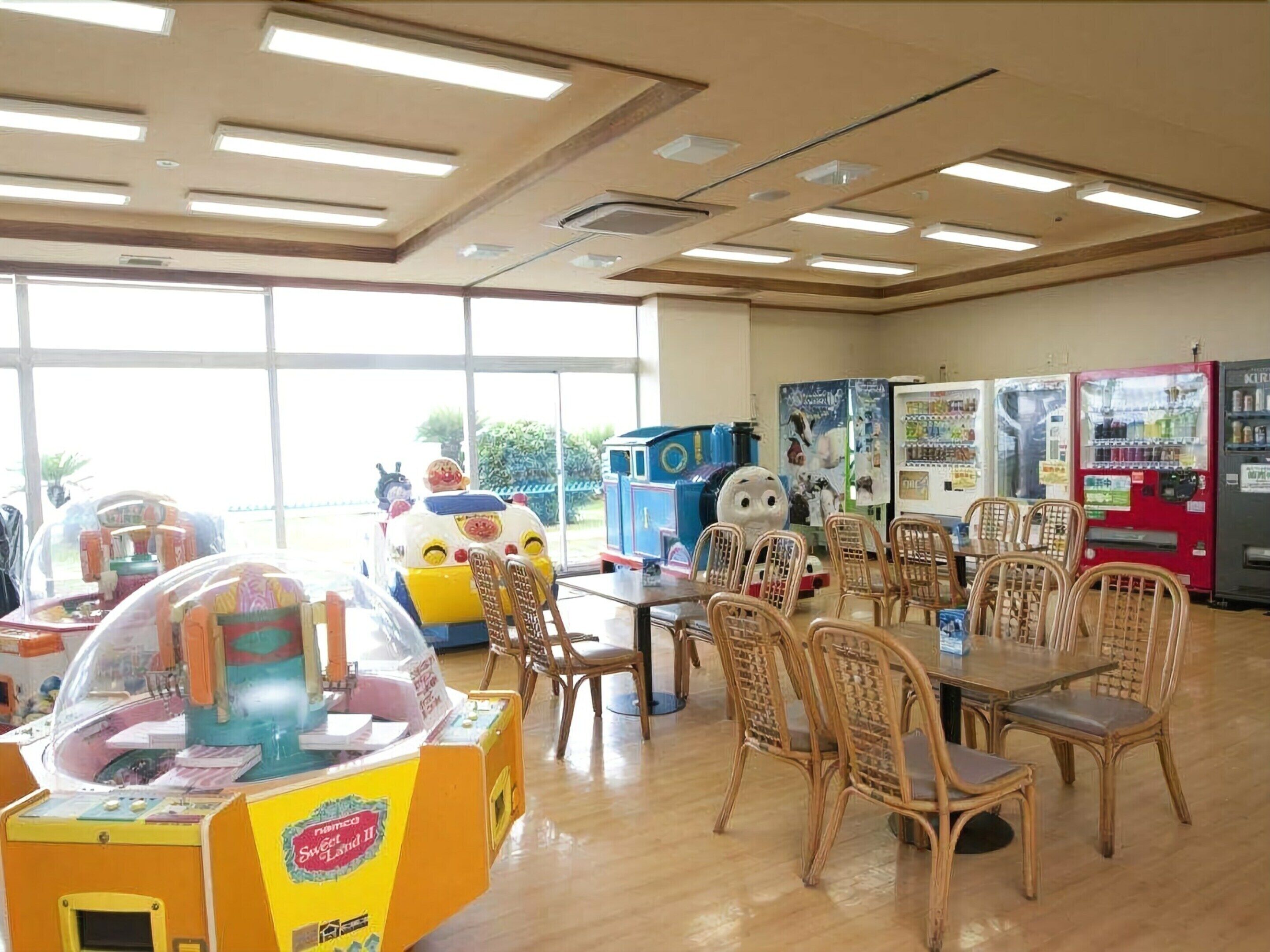 A room with a large window, wooden flooring, a table with chairs, and vending machines.