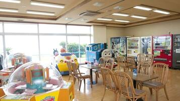 A room with a large window, wooden flooring, a table with chairs, and vending machines.