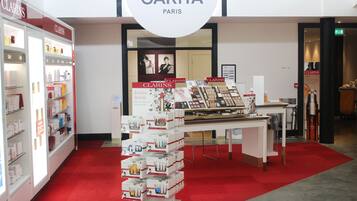 Een winkelinterieur met een rode loper, een displaytafel met diverse producten, en een bordje dat 'CARITA PARIS' vermeldt.