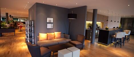 A modern living room with a sofa, ottomans, and a coffee table. There is a kitchen area in the background with a bar and stools.