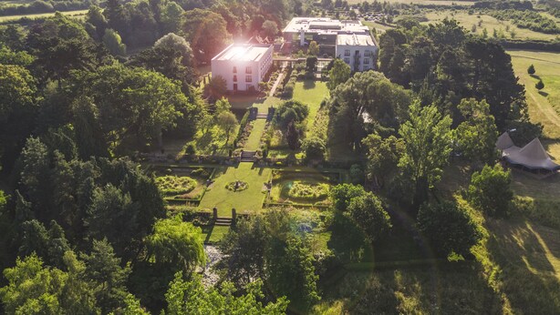 An aerial view of a property with a central building surrounded by manicured gardens, a small pond, and a tent-like structure. - Lifehouse Spa & Hotel (Clacton-on-Sea)