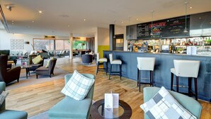 A modern bar area with a high bar counter, seating with bar stools, and a menu board. - Lifehouse Spa & Hotel (Clacton-on-Sea)