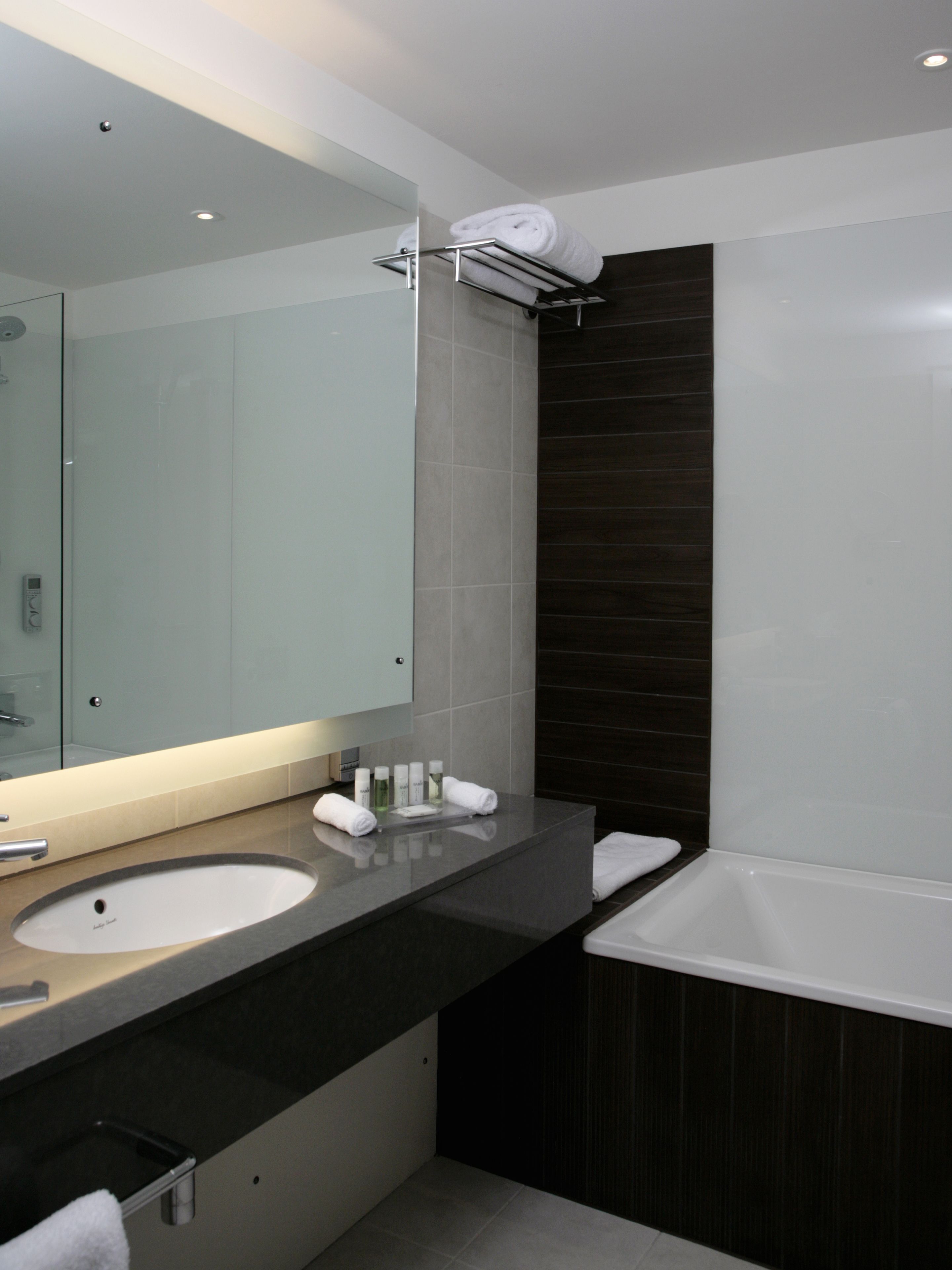 Une salle de bain moderne avec deux vasques, un grand miroir et un mur recouvert de carreaux foncés.
