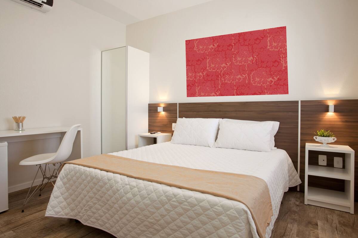 Ein modernes Hotelzimmer mit einem großen Bett, einem Schreibtisch, einem Stuhl und einem roten abstrakten Gemälde an der Wand.