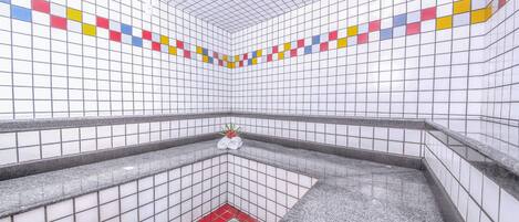 A tiled bathroom with a red floor and a small plant on the wall.
