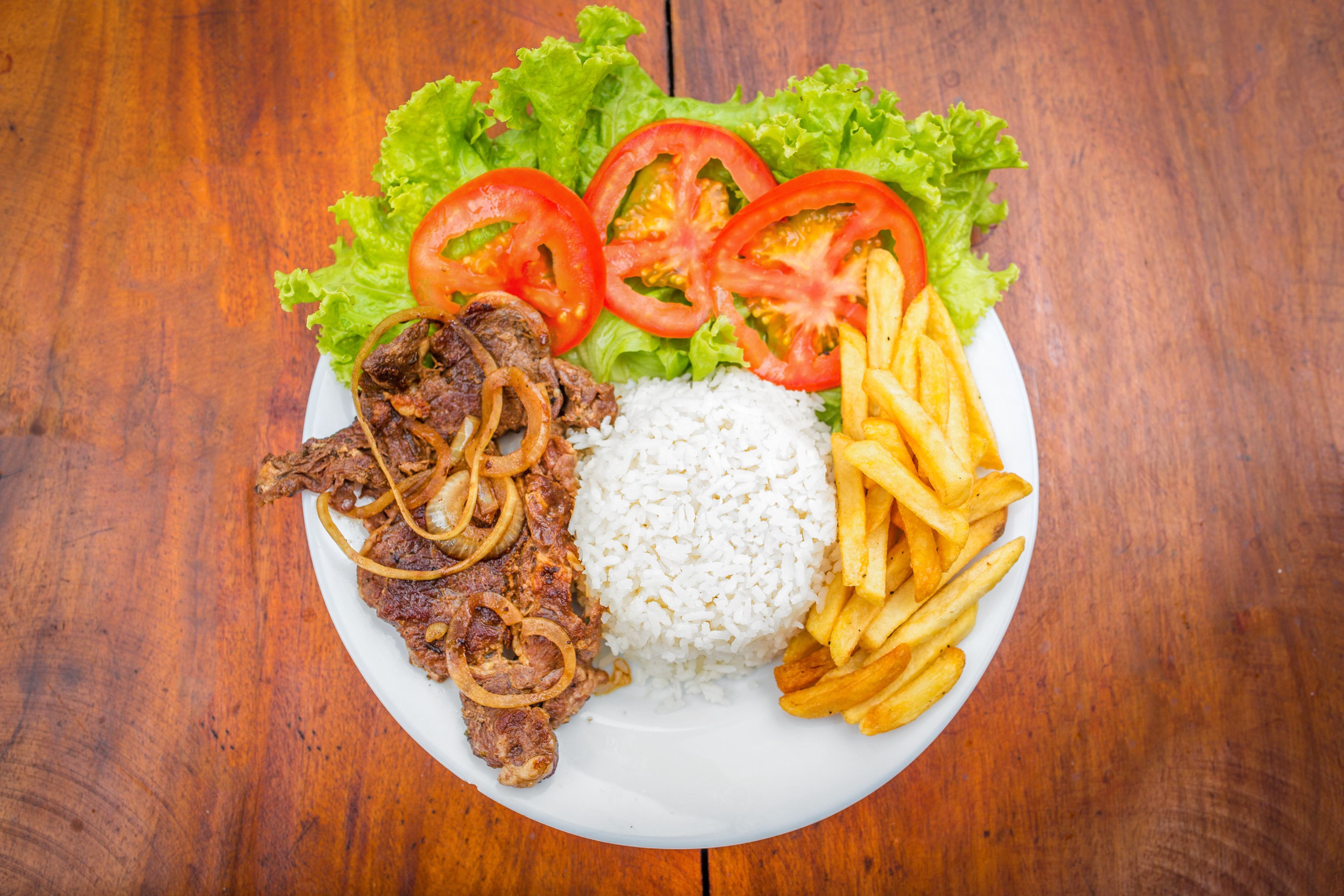 Um prato com carne, arroz, batatas fritas e alface com rodelas de tomate.