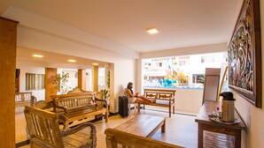 A spacious lobby with wooden furniture, a table with a kettle, and a view of a colorful outdoor area. - Shangrilá - Rede Soberano (Porto Seguro)