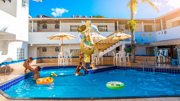 A swimming pool area with a statue, lounge chairs, and a palm tree. - Shangrilá - Rede Soberano (Porto Seguro)