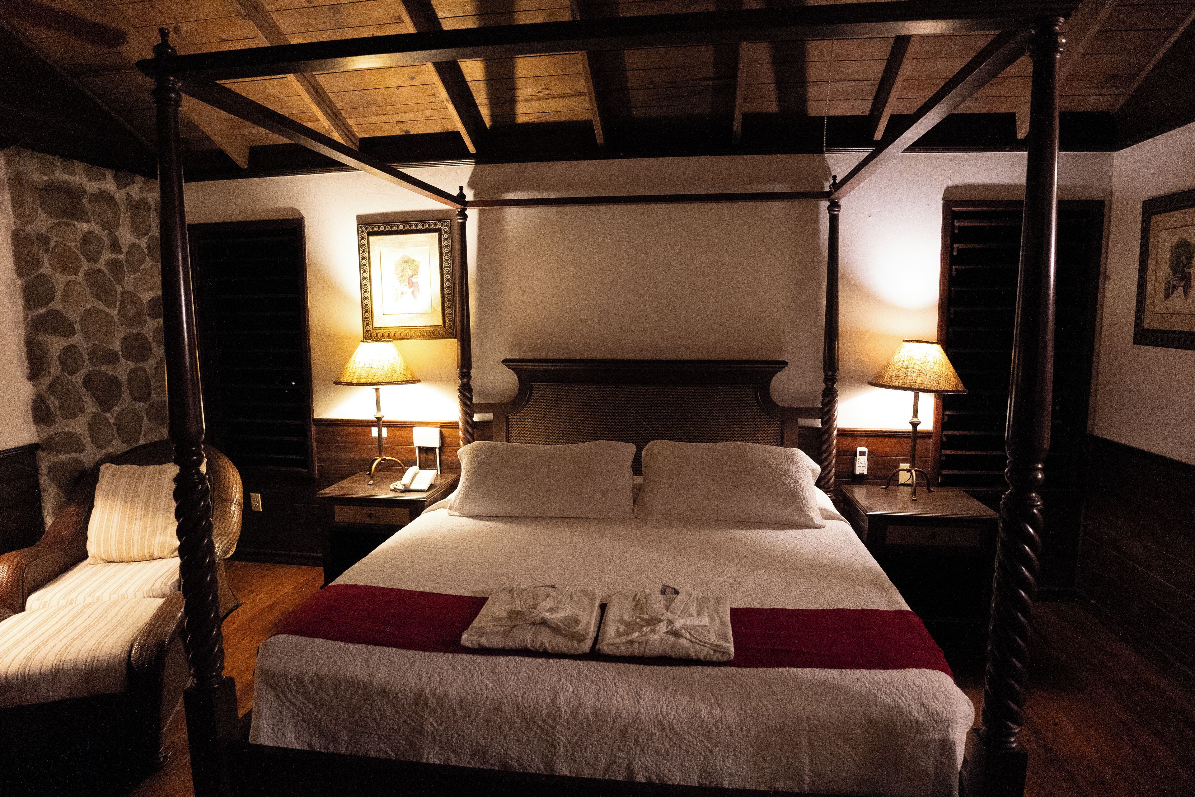A four-poster bed with white linens and a red throw blanket, flanked by two nightstands with lamps.