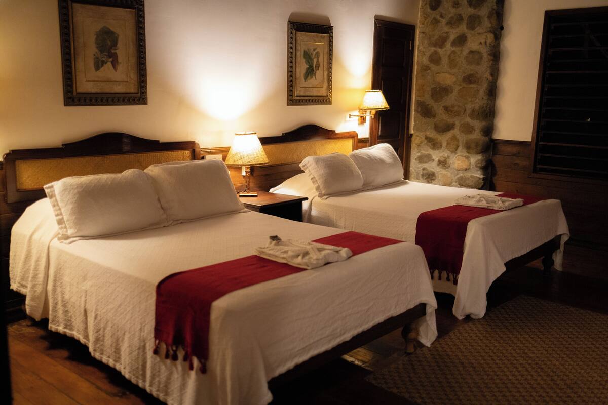 Two neatly made beds with white linens and red blankets, a wooden headboard, and a stone pillar.