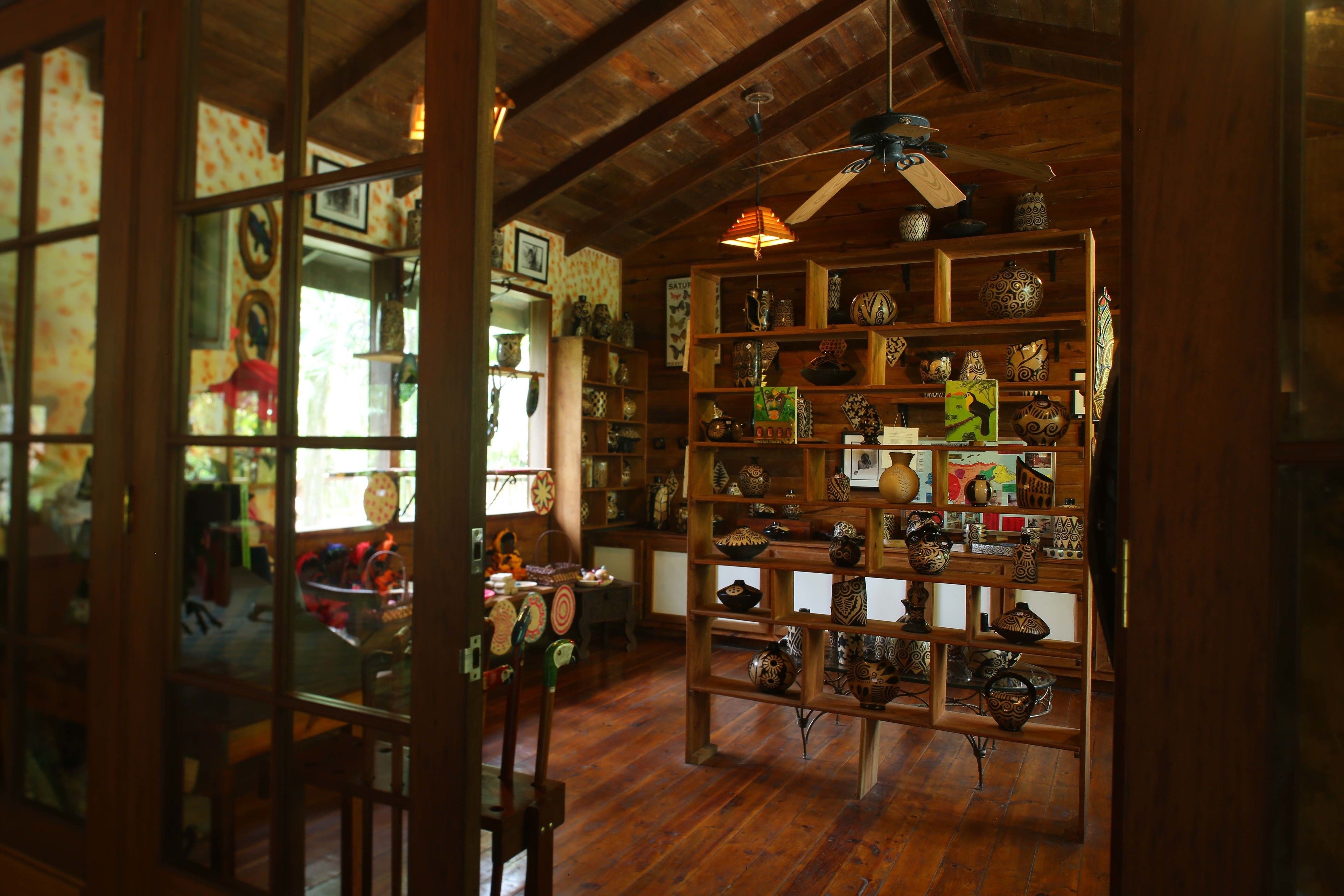 A room with wooden floors, a ceiling fan, and shelves filled with pottery.