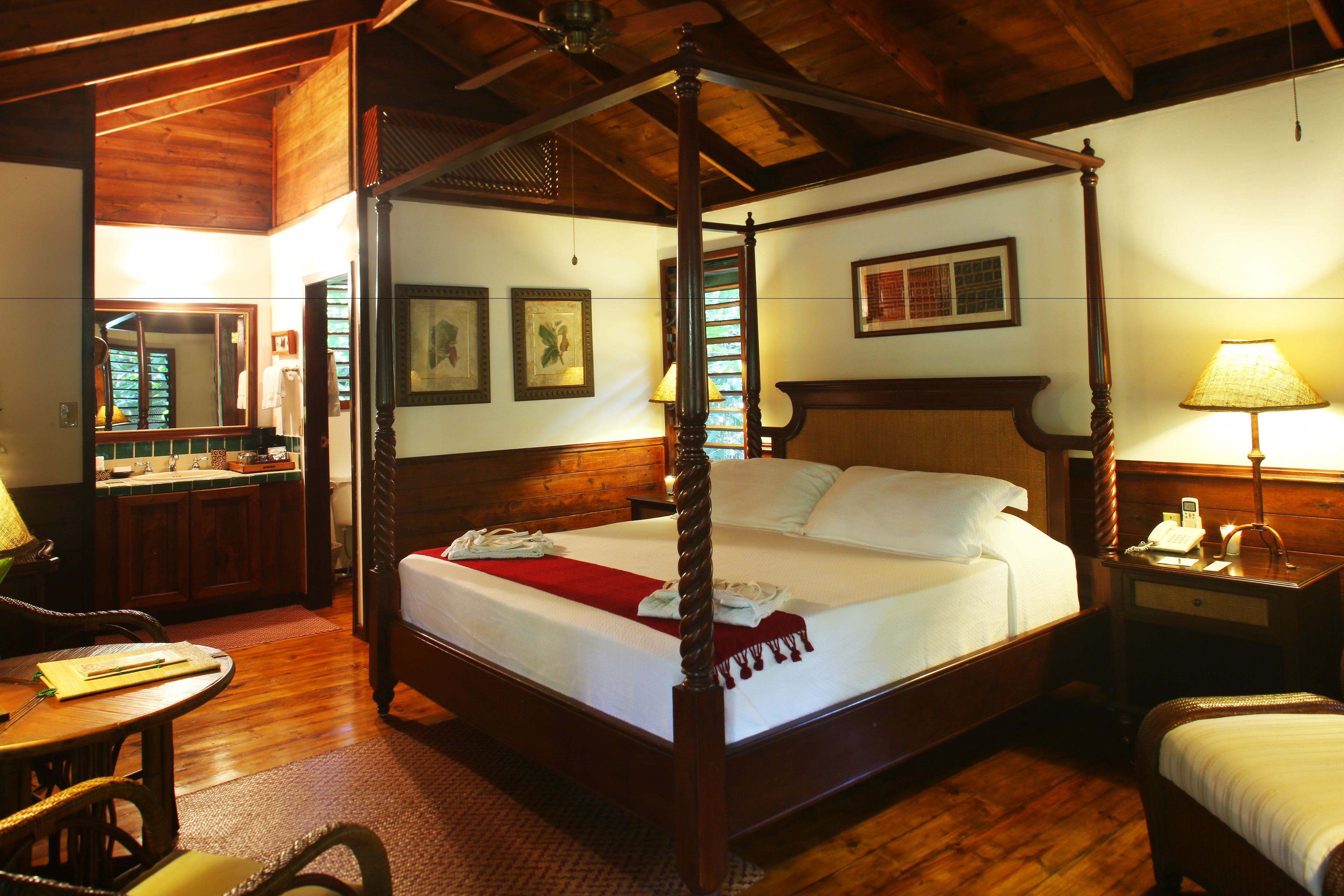 A four-poster bed with a wooden headboard, a bedside table with a lamp, and a mirror on the wall.