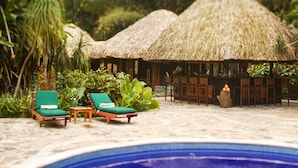 A poolside area with lounge chairs and a thatched-roof structure.