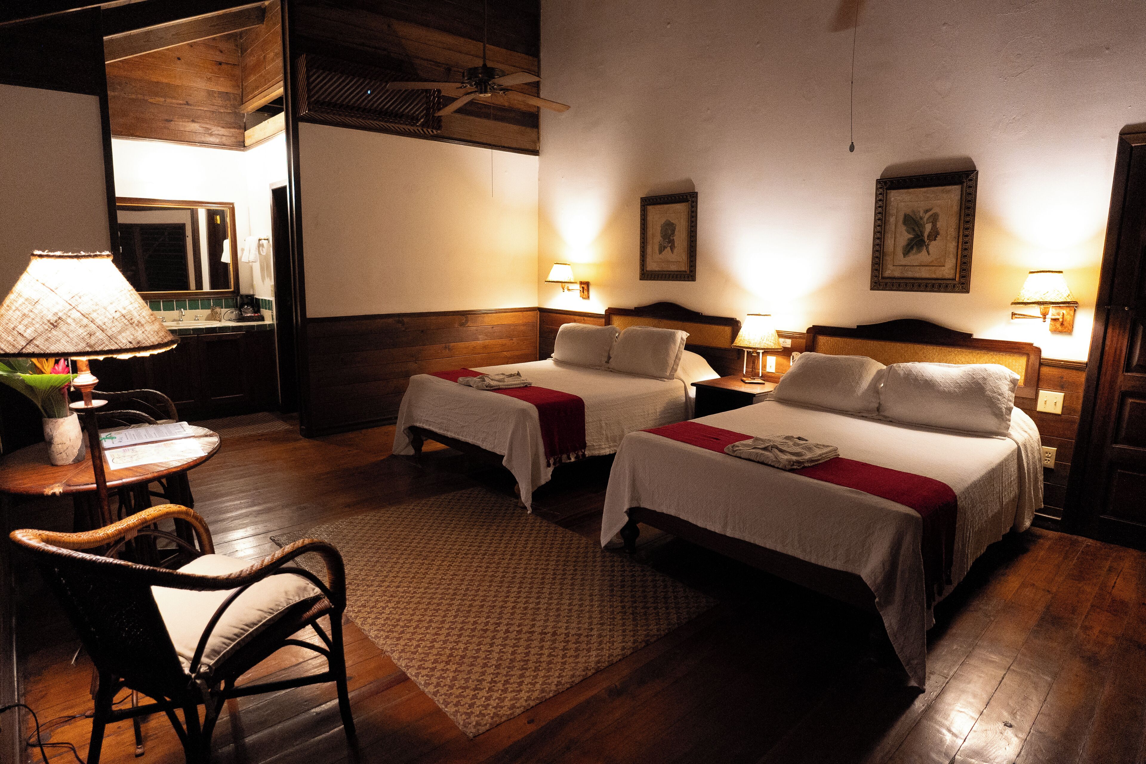 A hotel room with two beds, a sitting area with a chair, a small table, and a lamp.