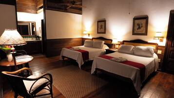 A hotel room with two beds, a sitting area with a chair, a small table, and a lamp.