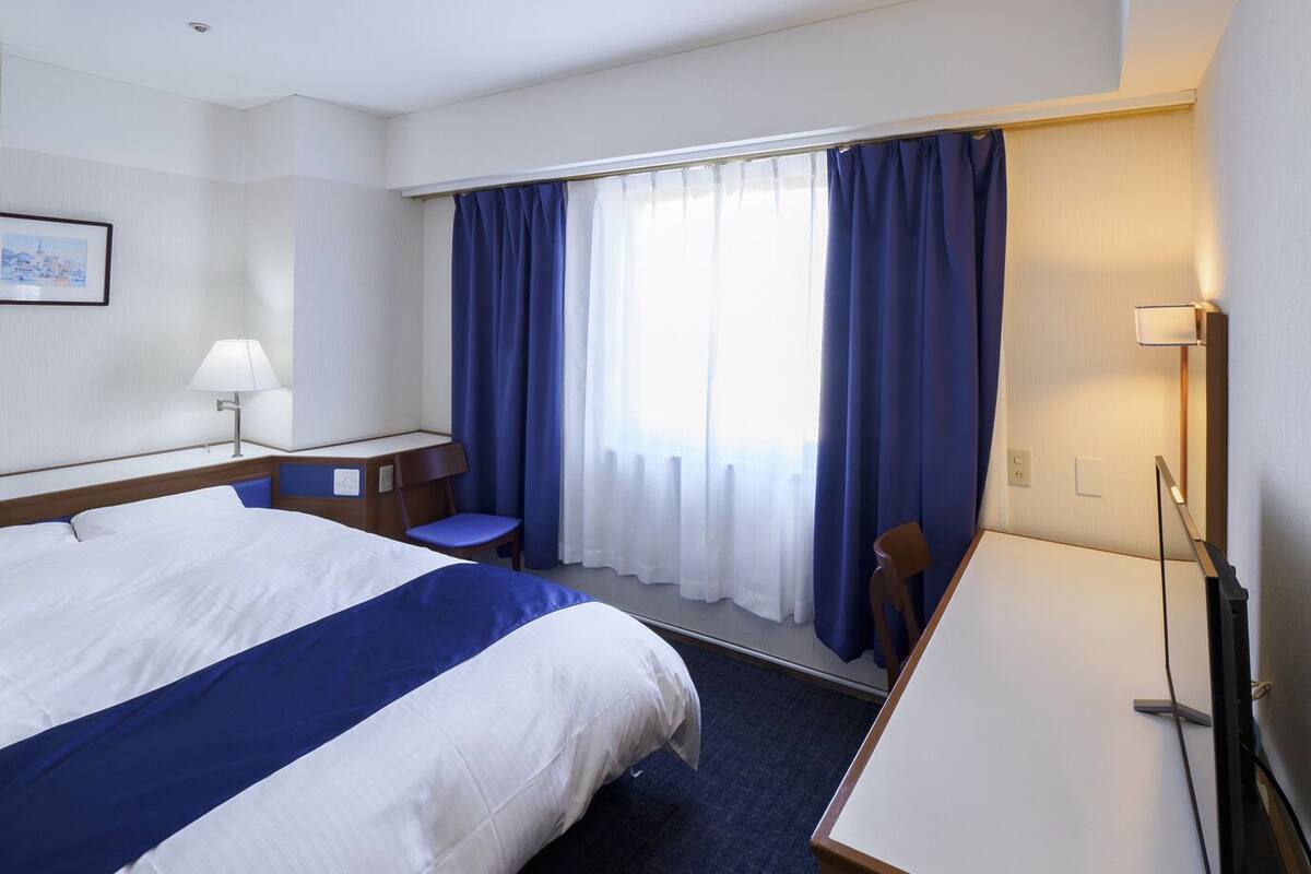 A hotel room with a large bed, a desk, a chair, and a desk lamp.