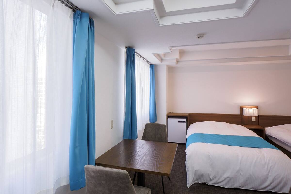 A hotel room with two beds, a desk, a chair, and a small table.