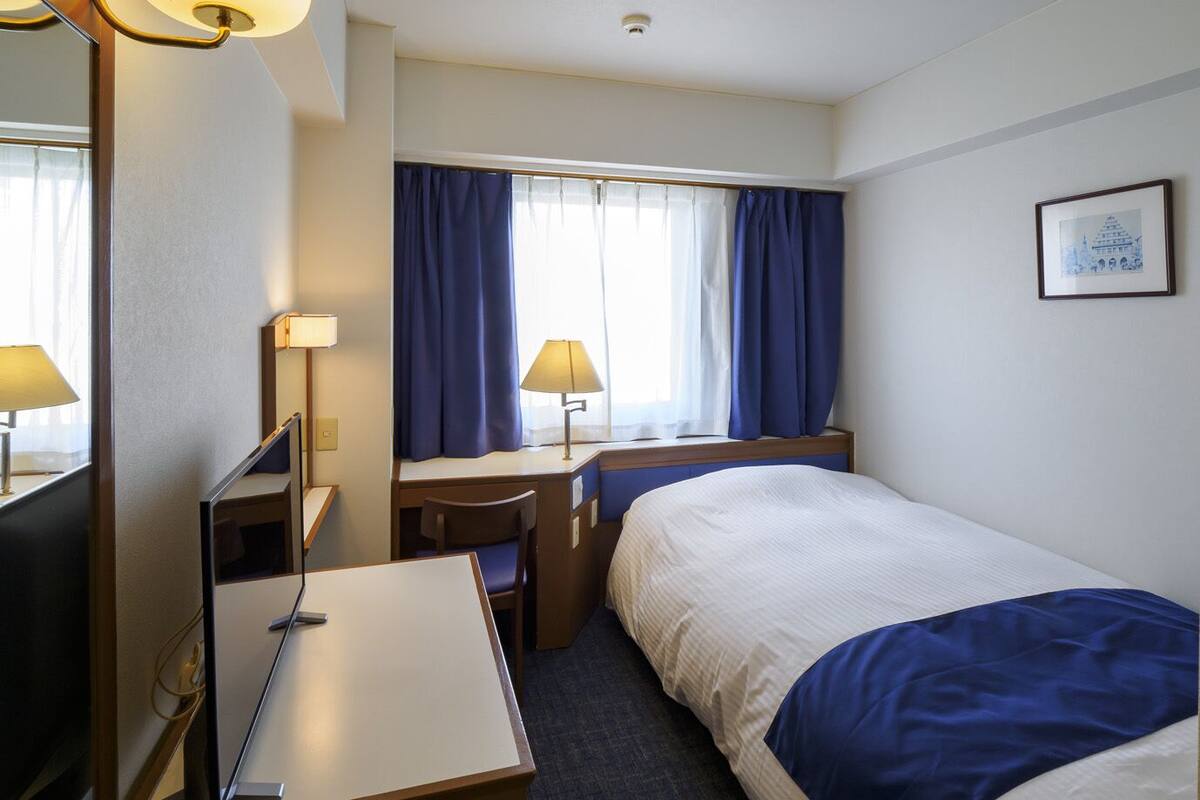 A hotel room with a bed, desk, chair, and two lamps.