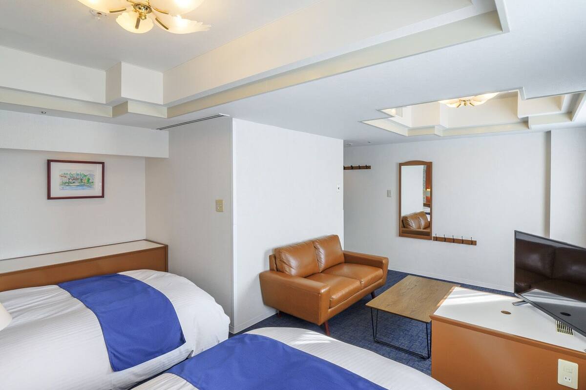 A hotel room with two beds, a sofa, a desk, a television, and a ceiling fan.