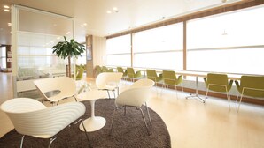 A modern interior with a large window, white chairs, a round table, and a potted plant. - Hotel Premium Green Hills (Sendai)