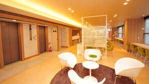 A modern hotel lobby with a reception desk, seating area, and elevators. - Hotel Premium Green Hills (Sendai)