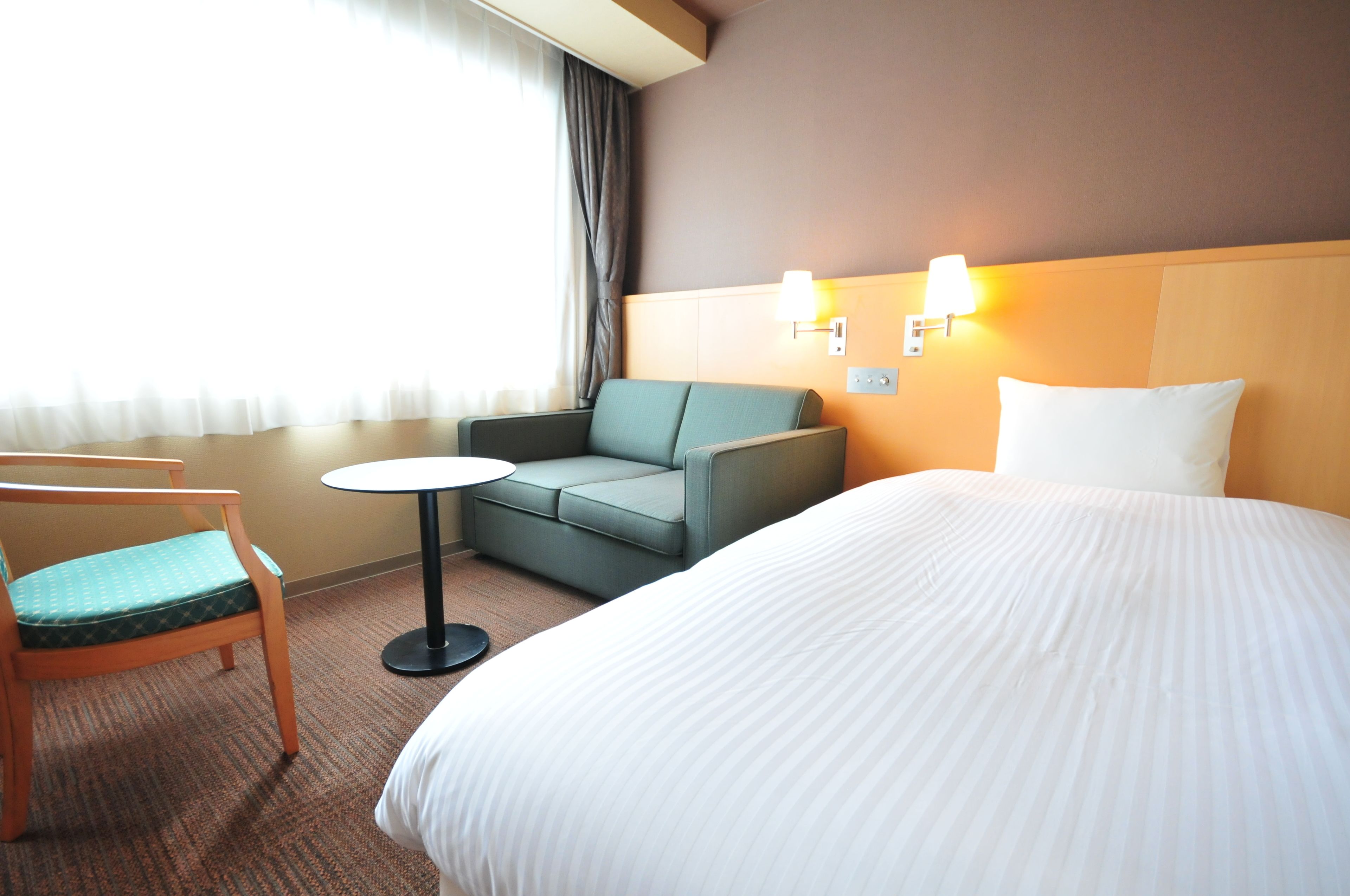A hotel room with a bed, a green sofa, a small round table, and a wooden chair.