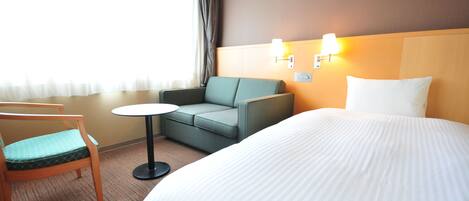 A hotel room with a bed, a green sofa, a small round table, and a wooden chair.