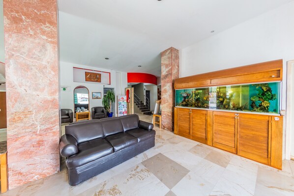 A lobby with a black leather sofa, marble columns, a wooden cabinet with a fish tank, and a staircase in the background. - Hotel Ziami (Veracruz)