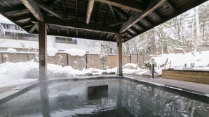 A hot tub area with a tiled floor and a wooden roof structure. - Kurobe Kanko Hotel (Omachi)