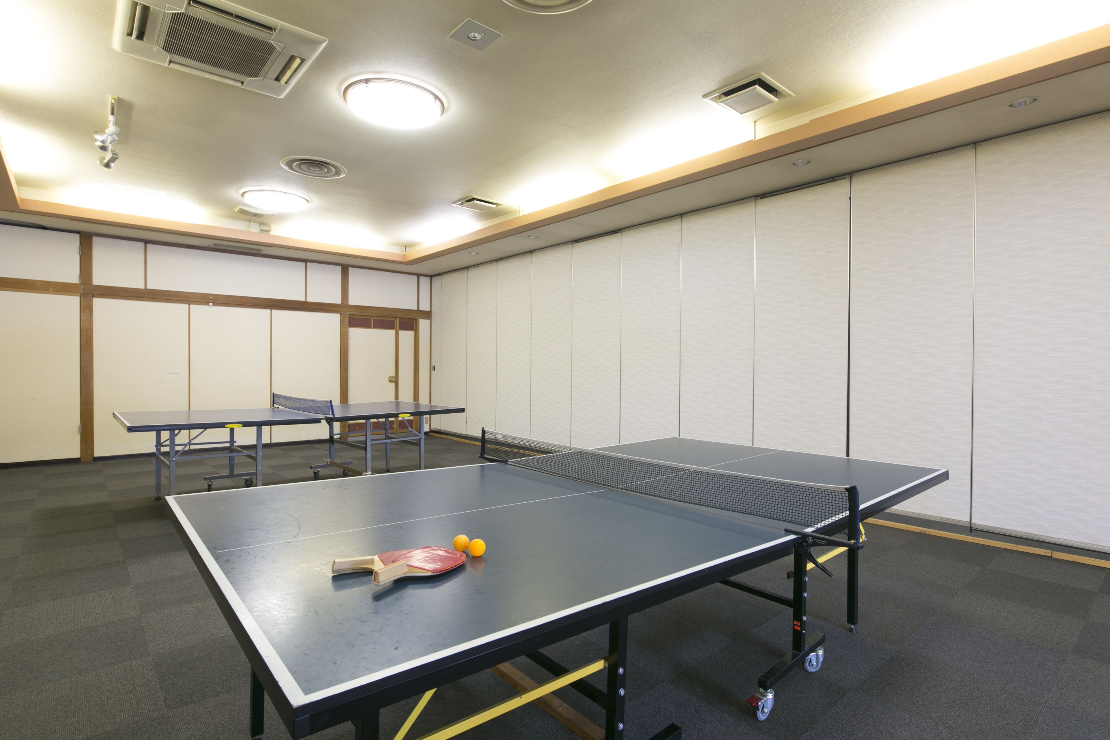 Une table de ping-pong avec une raquette et des balles, une table plus petite et un mur avec des panneaux.