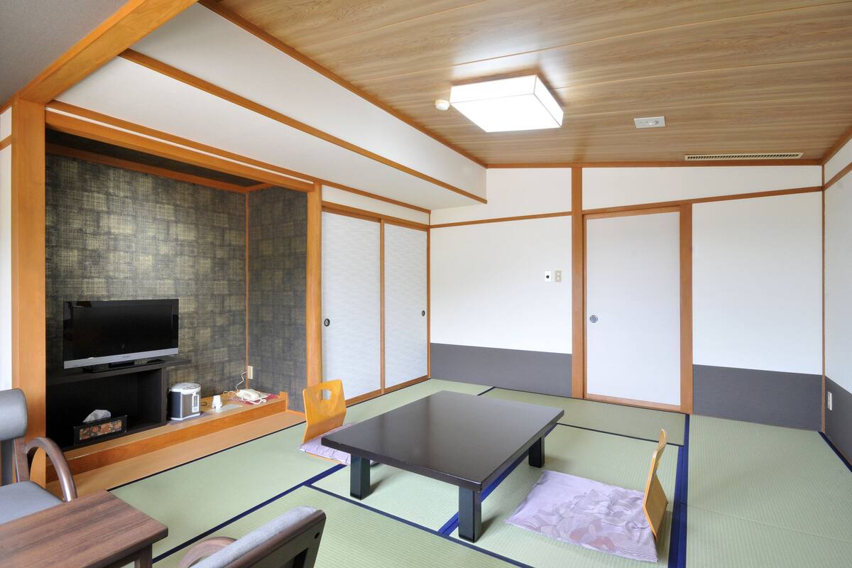 A traditional Japanese room with tatami flooring, a low table, a television, and sliding doors.