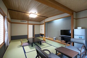 A traditional Japanese-style room with tatami flooring, a low table, a cushioned chair, a television, and a refrigerator. - Kurobe Kanko Hotel (Omachi)