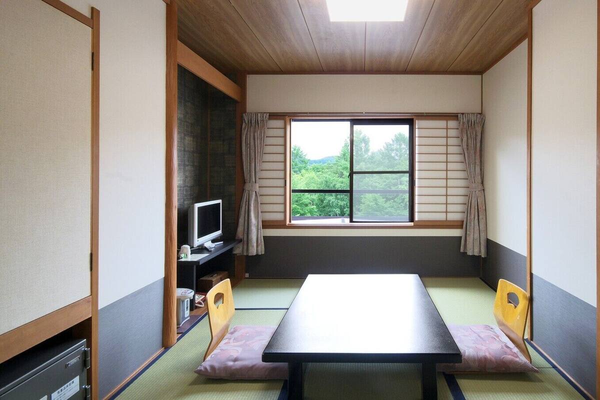 A traditional Japanese room with tatami flooring, a low table, and a television on a stand.